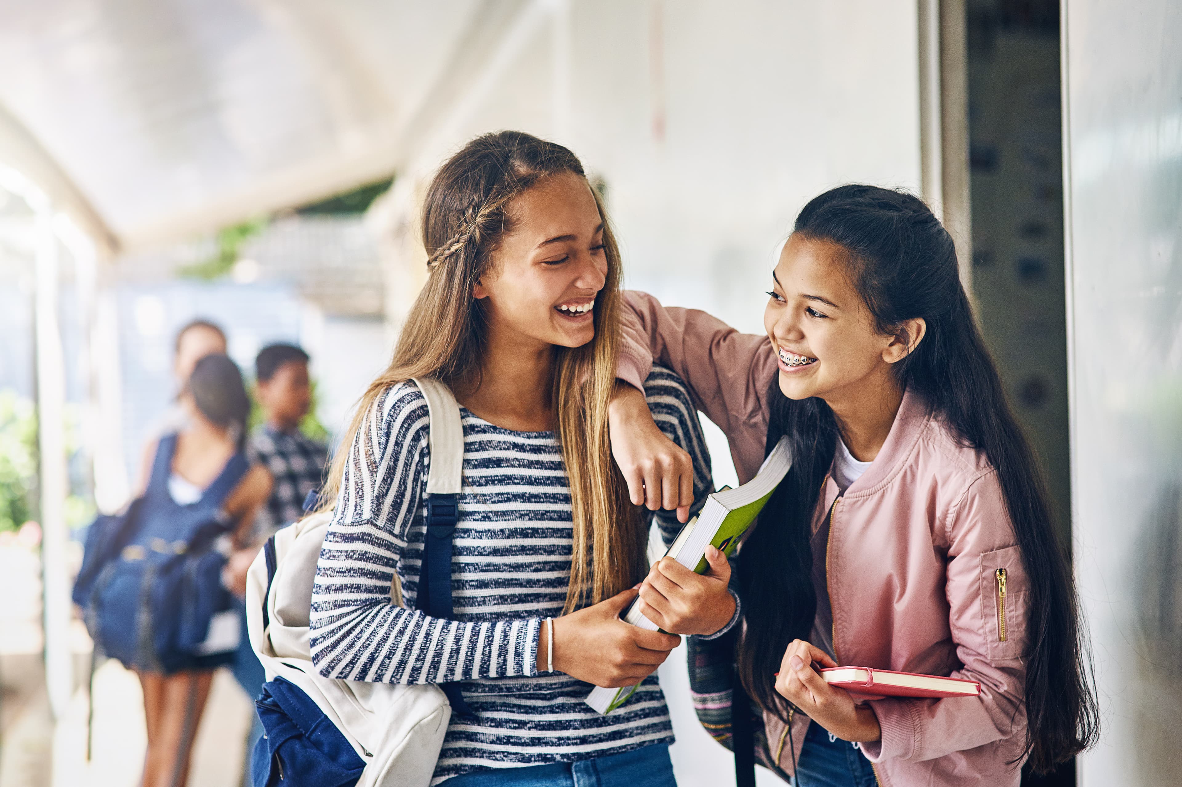 Shot of two happy schoolgirls chatting in the hallway outside their classroom