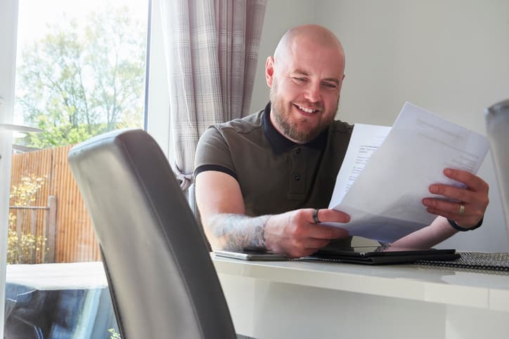 A male homeowner sits at the dining table reading through the latest household bills.