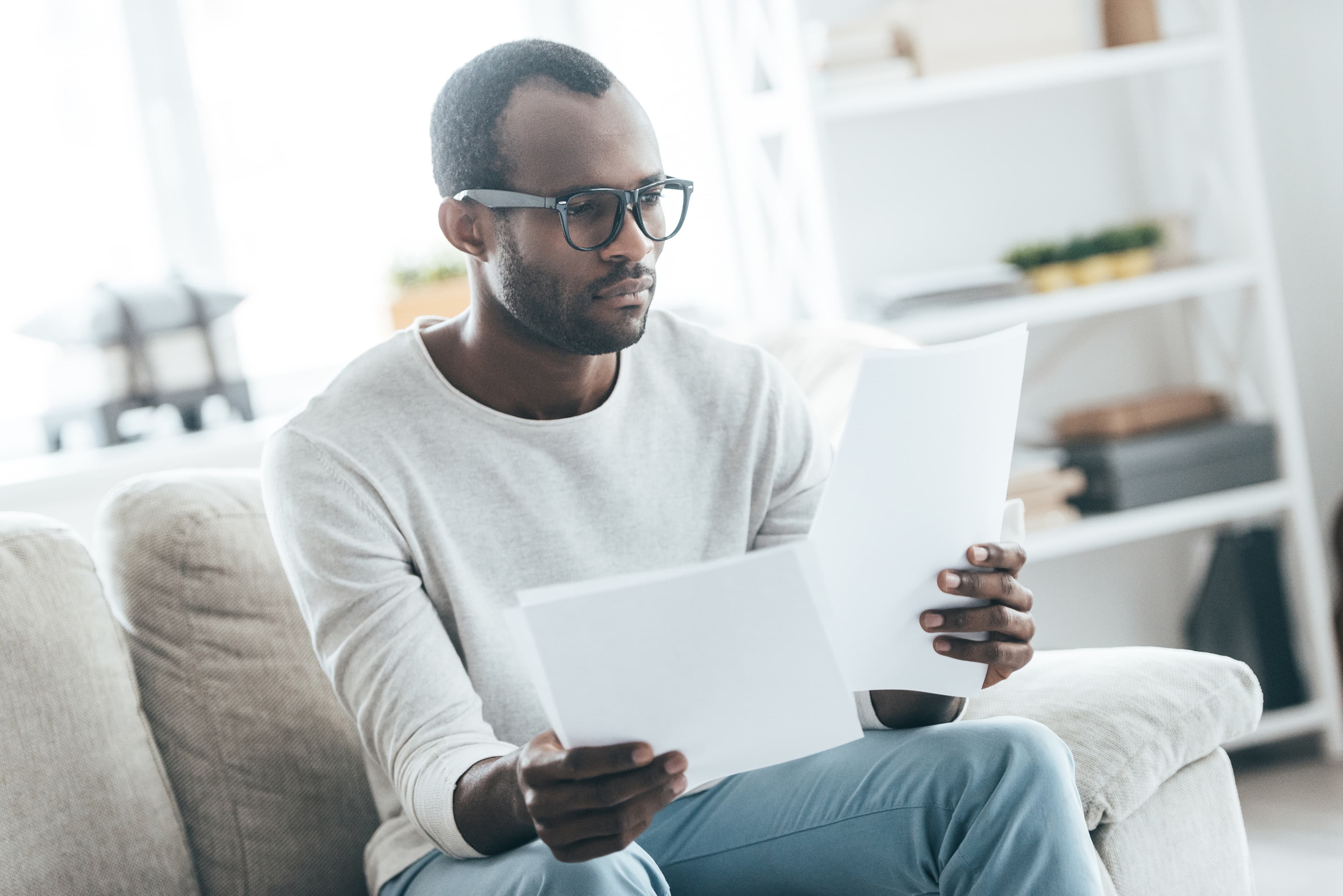 Handsome young African man working with documents while sitting on the sofa at home