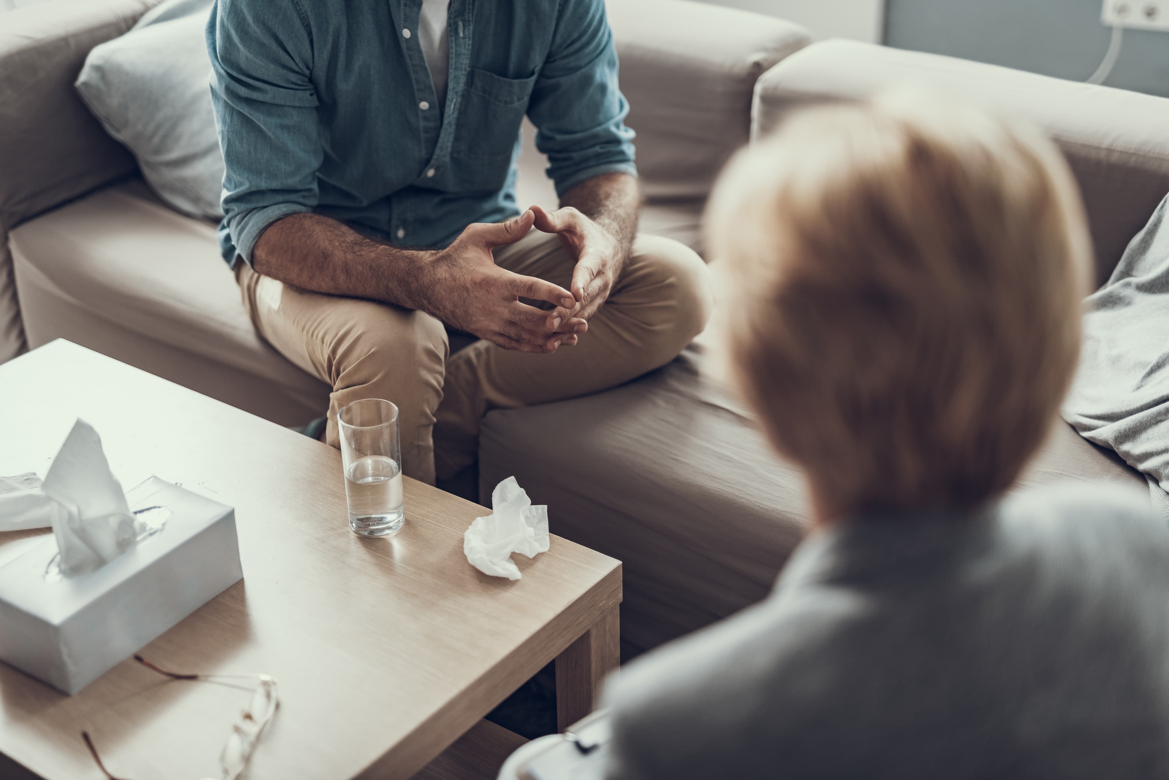 Man sitting on the sofa with his hands together and his psychotherapist sitting in front of him