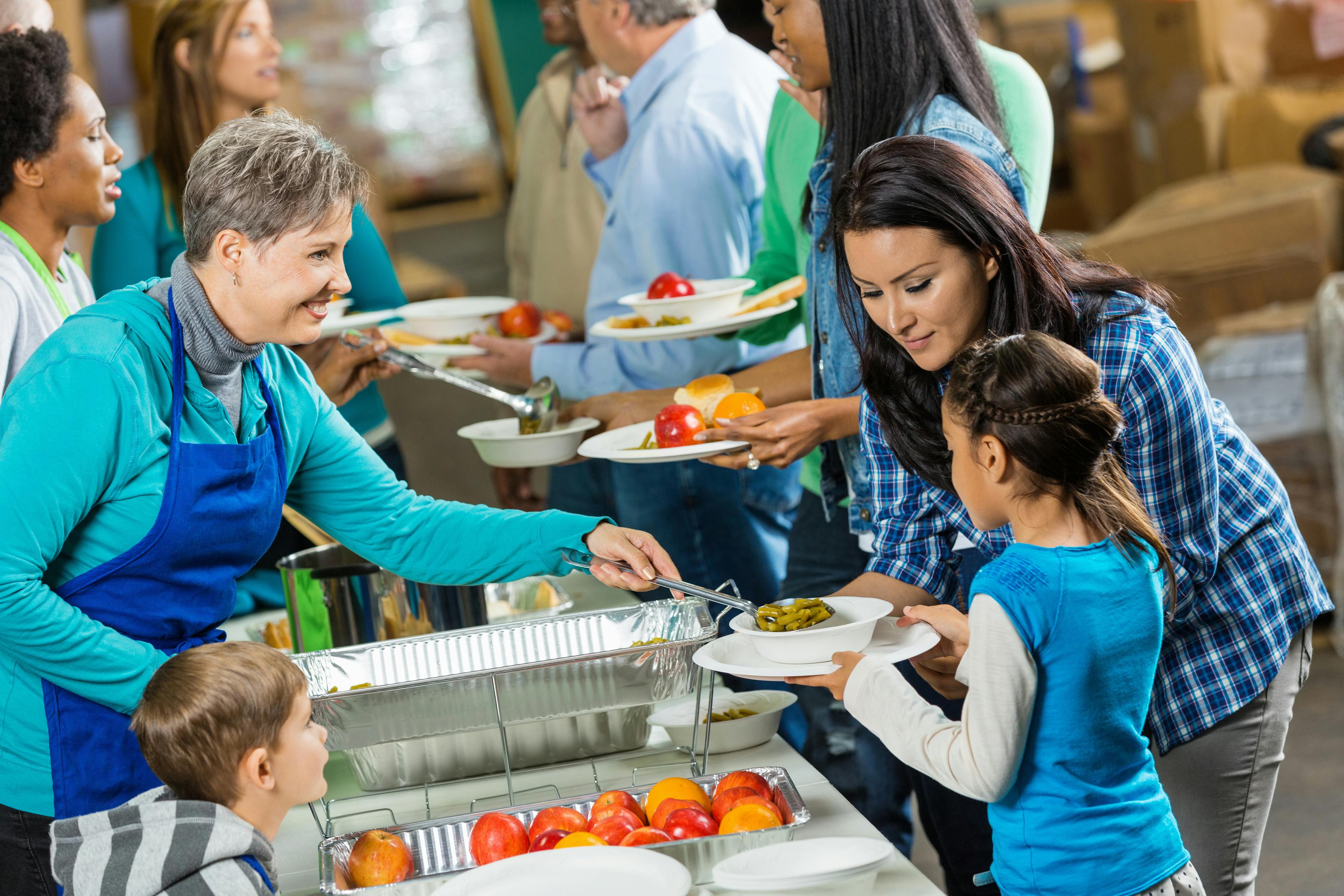 Senior volunteer serving healthy meal to family at soup kitchen