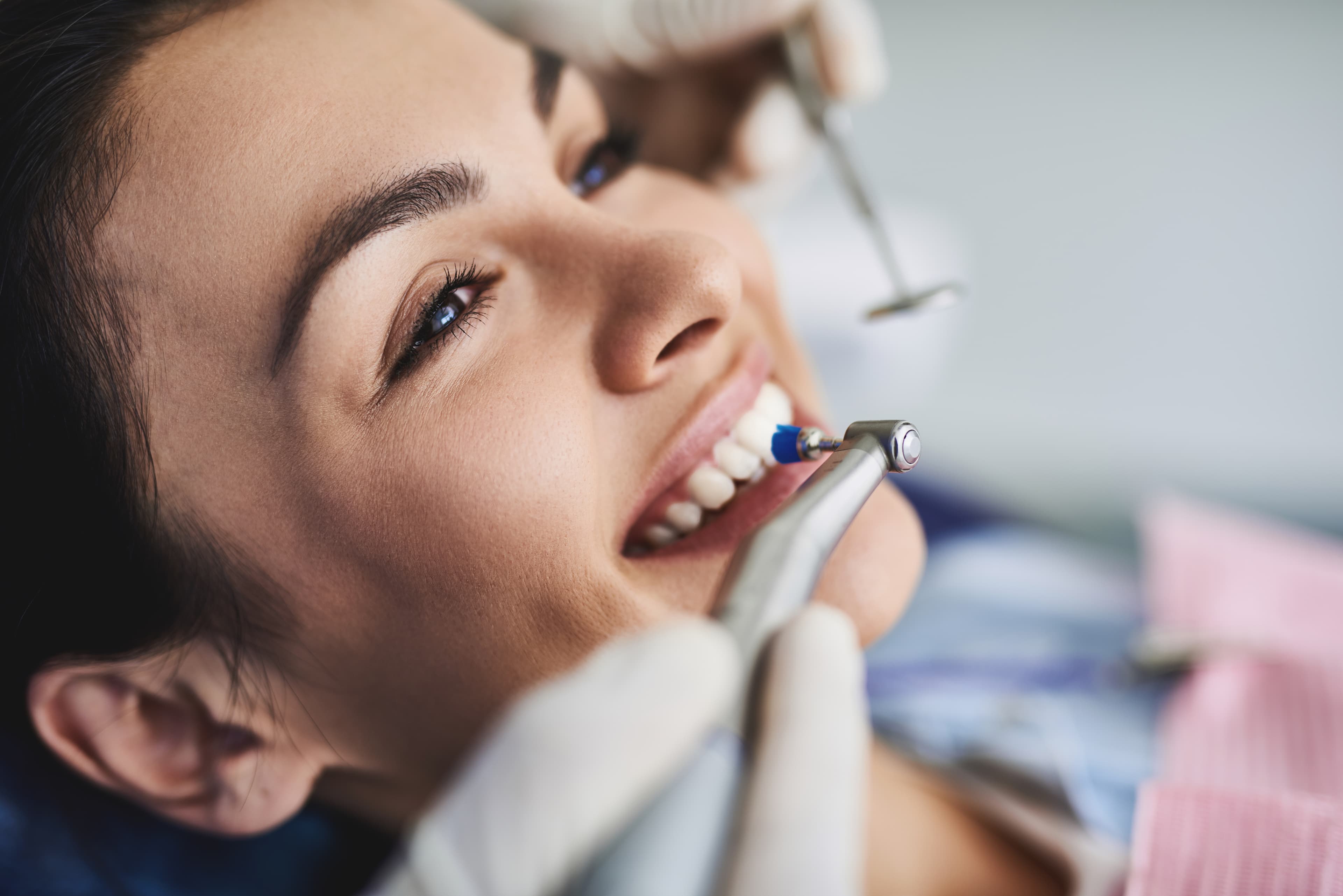 Close up portrait of pretty girl sitting in dental chair while stomatologist holding polisher and mirror. Girl is smiling