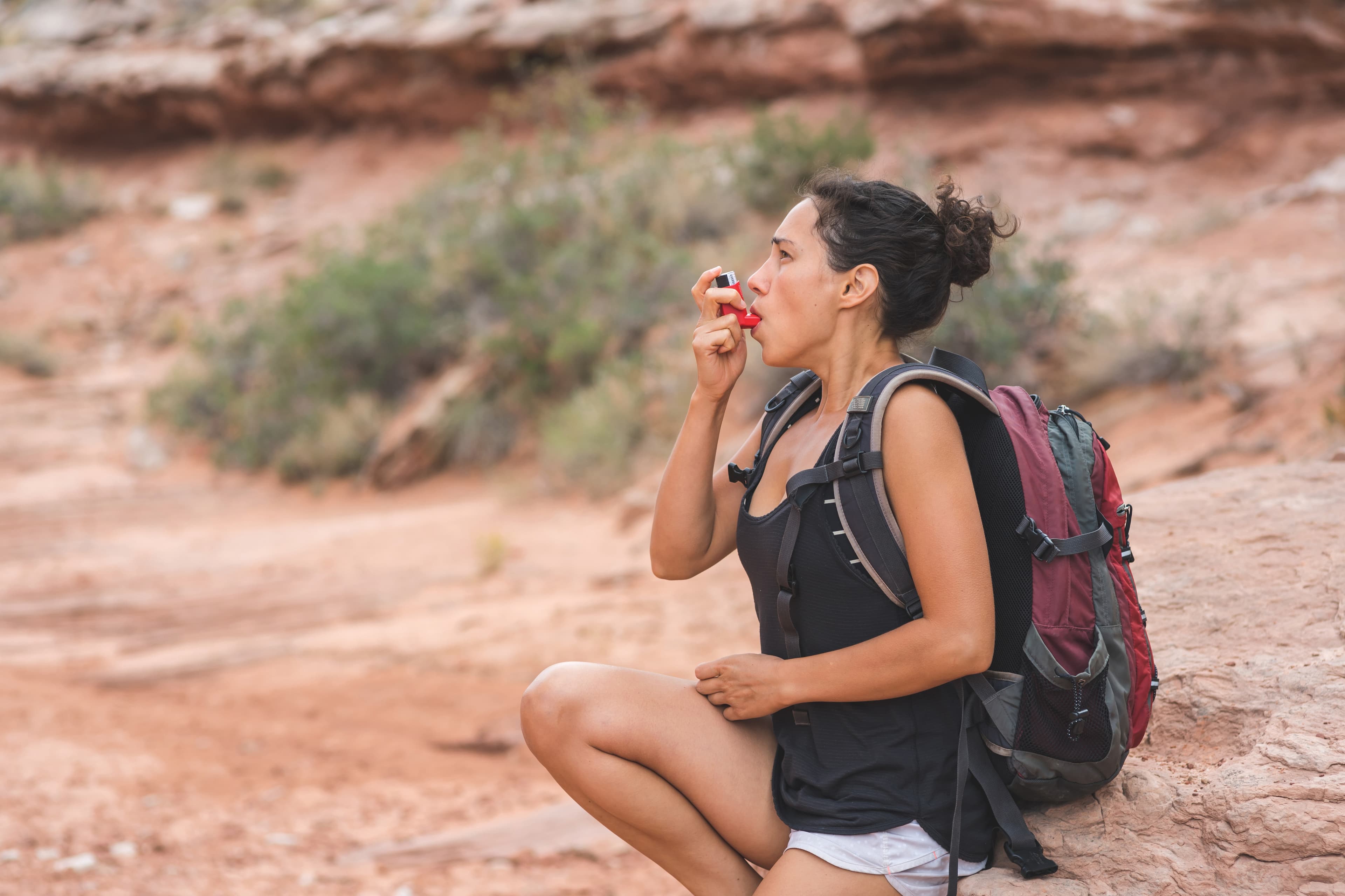 A young ethnic female takes a short break from her day hike in the Utah desert to use her inhaler for her chronic asthma.